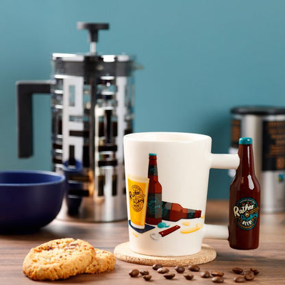 Cană ceramică 3D 'I'd Rather Be Drinking Beer', design amuzant, toartă inedită, lângă biscuiți și cafea.